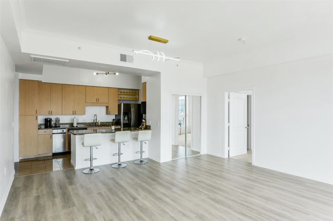 Kitchen with black refrigerator with ice dispenser, a kitchen bar, dark countertops, light wood finished floors, and dishwasher | Image 16