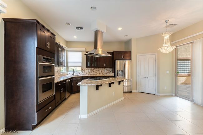 Kitchen featuring tasteful backsplash, a breakfast bar area, stainless steel appliances, island exhaust hood, and a sink | Image 9