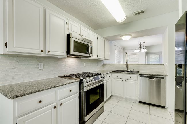 Kitchen with light tile patterned floors, an inviting chandelier, visible vents, a sink, and stainless steel appliances | Image 14