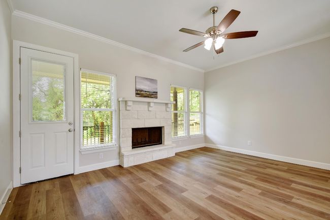 Unfurnished living room featuring a stone fireplace, wood finished floors, crown molding, plenty of natural light, and a ceiling fan | Image 5