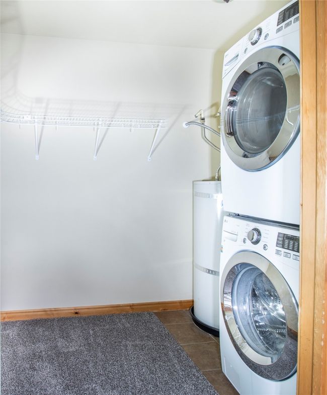 Laundry room featuring stacked washing machine and dryer, strapped water heater, and dark tile patterned floors | Image 17