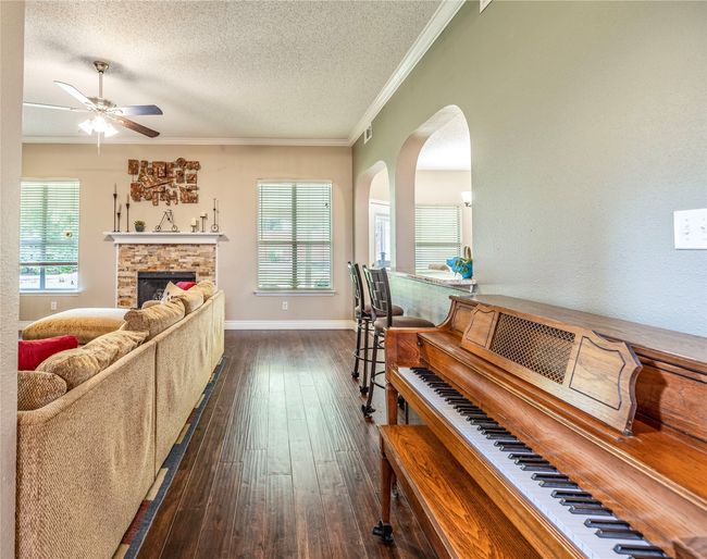 Living room with ceiling fan, ornamental molding, dark wood-type flooring, a textured ceiling, and arched walkways | Image 10