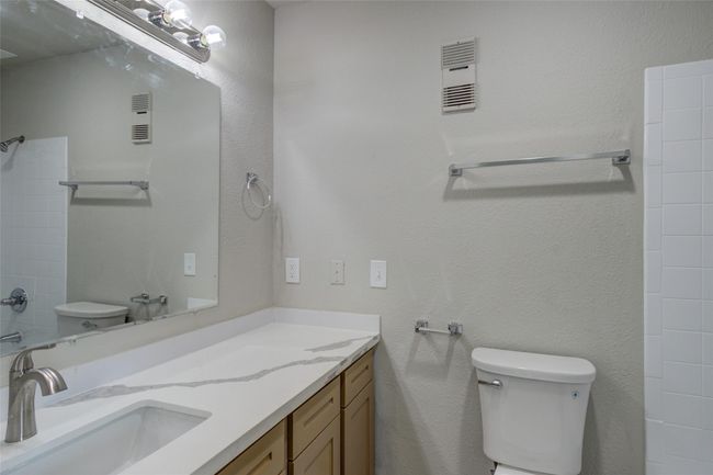 Modern bathroom with a large mirror, sleek white countertop, and ample cabinet space. Features include a standard toilet and a bathtub with tiled walls. | Image 20