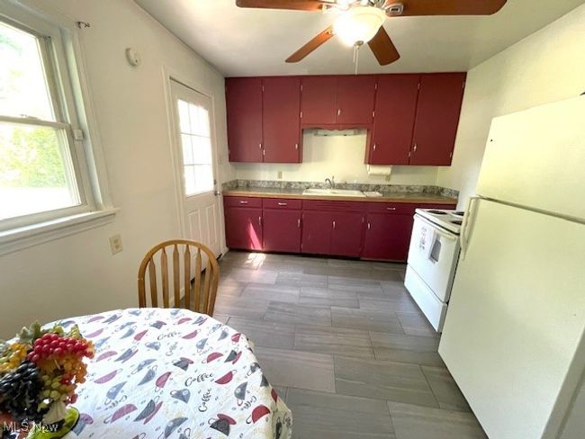Kitchen featuring white appliances, red cabinetry, a ceiling fan, and a sink | Image 4