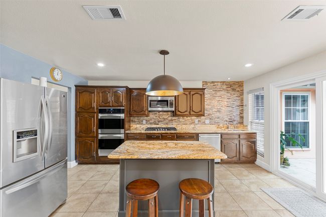 Kitchen featuring visible vents, light tile patterned floors, appliances with stainless steel finishes, and decorative backsplash | Image 9