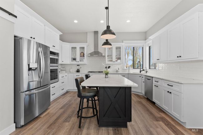 Kitchen featuring appliances with stainless steel finishes, wall chimney range hood, decorative backsplash, white cabinetry, and glass insert cabinets | Image 18