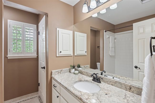 Full bath with granite countertop, white cabinetry, plantation shutters, and a tiled shower/tub combo. | Image 23