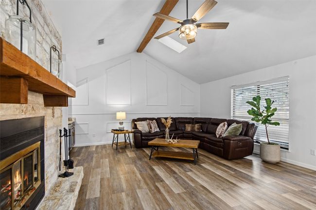 Living area featuring wood finished floors, a stone fireplace, a ceiling fan, and a skylight | Image 9
