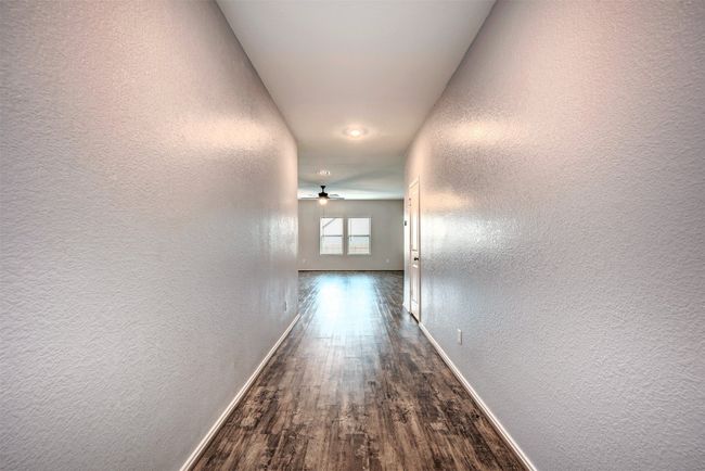 Hall featuring a textured wall, baseboards, and dark wood-style floors | Image 5