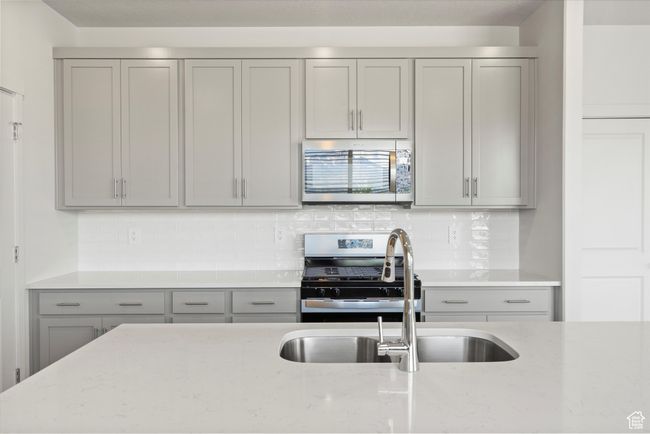 Kitchen with appliances with stainless steel finishes, gray cabinetry, light stone counters, and tasteful backsplash | Image 23