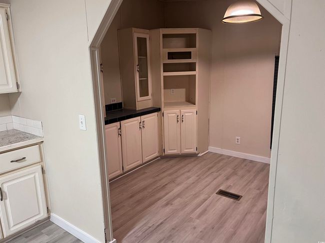 Kitchen with light wood finished floors, baseboards, open shelves, and white cabinetry | Image 13