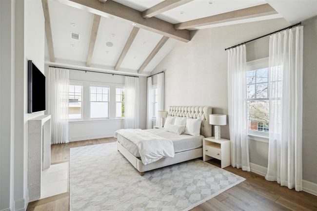 Upstairs, a breathtaking primary suite awaits, featuring gleaming oak hardwood floors and a striking ceiling adorned with white pine beams. This luxurious retreat is centered around an exquisite gas log fireplace with a custom stone mantel and boasts a spa-like marble bath with a spacious walk-in closet. | Image 14