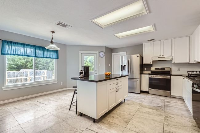 Kitchen featuring appliances with stainless steel finishes, under cabinet range hood, dark countertops, and light marble finish flooring | Image 10