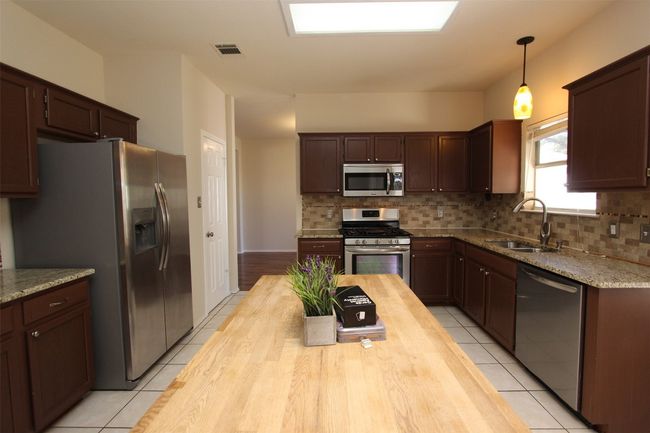 Kitchen featuring appliances with stainless steel finishes, butcher block counters, light tile patterned floors, and tasteful backsplash | Image 5