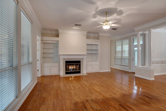 Unfurnished living room featuring ornate columns, ceiling fan, light wood-style flooring, ornamental molding, and a tiled fireplace | Image 5