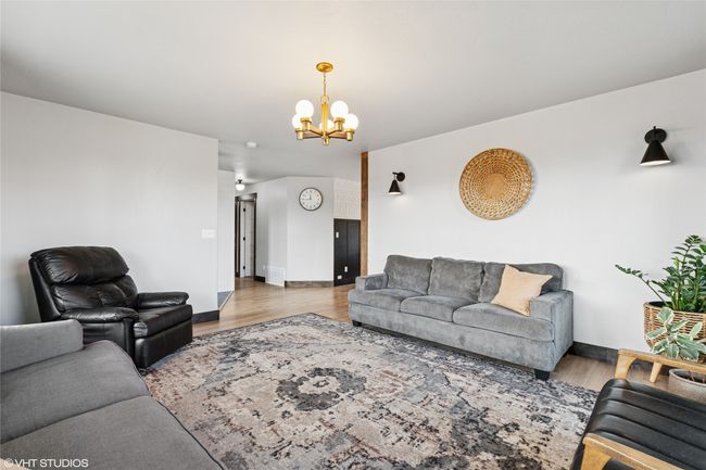 Living room with wood finished floors, a notable chandelier, and baseboards | Image 8