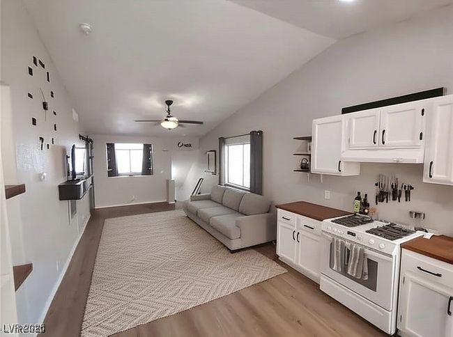Kitchen featuring white gas stove, light wood finished floors, white cabinets, open shelves, and lofted ceiling | Image 9