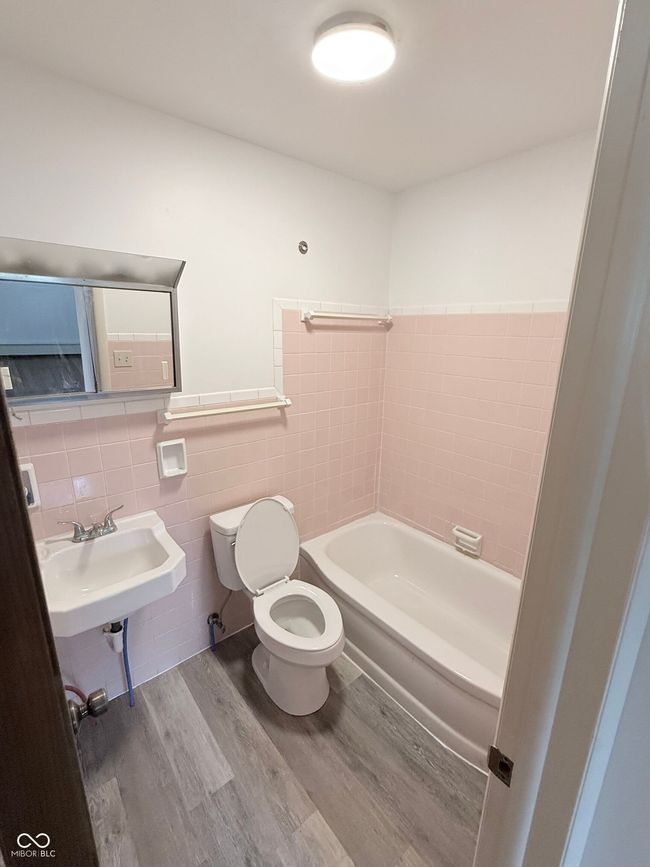 bathroom with a tub to relax in, wood finished floors, tile walls, and a wainscoted wall | Image 11