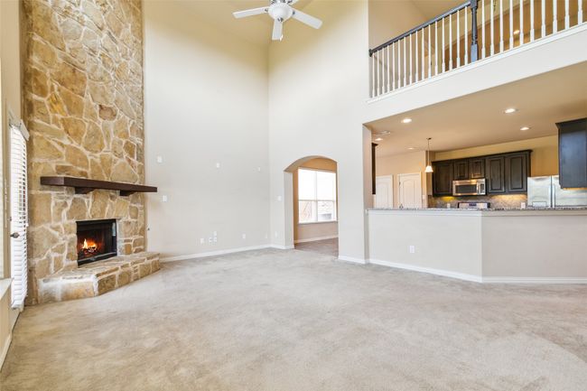 Unfurnished living room with light carpet, ceiling fan, arched walkways, a fireplace, and a towering ceiling | Image 8