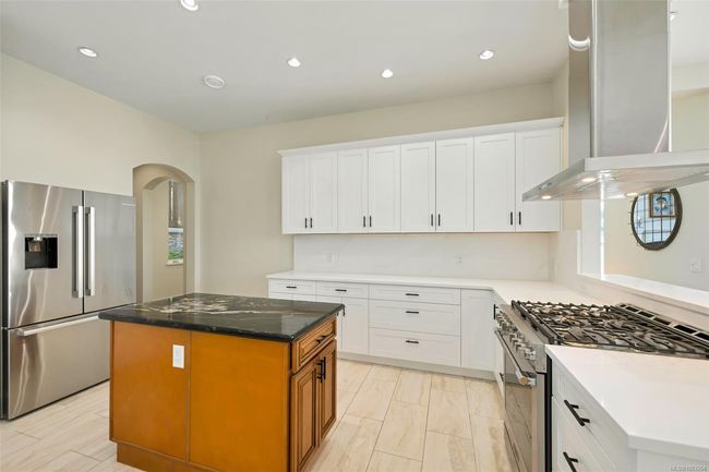 Kitchen with appliances with stainless steel finishes, wall chimney exhaust hood, arched walkways, white cabinetry, and a center island | Image 50