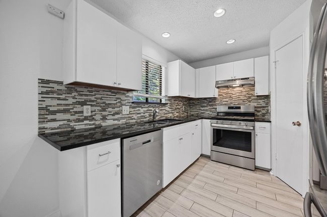Kitchen with stainless steel appliances, under cabinet range hood, a sink, and dark countertops | Image 11