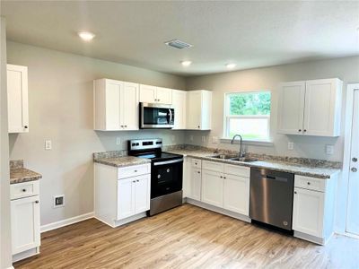 Kitchen with light stone counters, sink, white cabinetry, light hardwood / wood-style flooring, and appliances with stainless steel finishes | Image 3