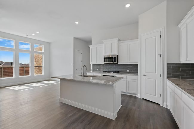 Kitchen with light stone countertops, dark wood finished floors, appliances with stainless steel finishes, white cabinets, and a sink | Image 7