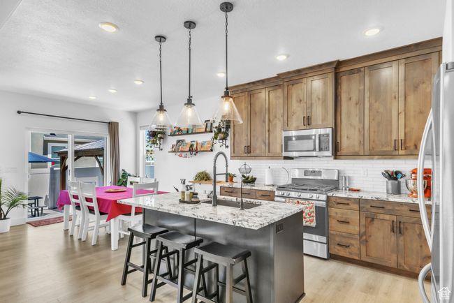 Kitchen with appliances with stainless steel finishes, tasteful backsplash, light wood-style floors, an island with sink, and brown cabinetry | Image 10