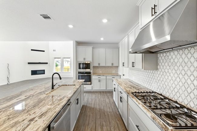 Kitchen featuring stainless steel appliances, under cabinet range hood, a sink, light stone counters, and recessed lighting | Image 13