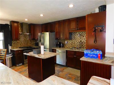 Kitchen with a kitchen island, decorative backsplash, sink, wall chimney range hood, and appliances with stainless steel finishes | Image 3