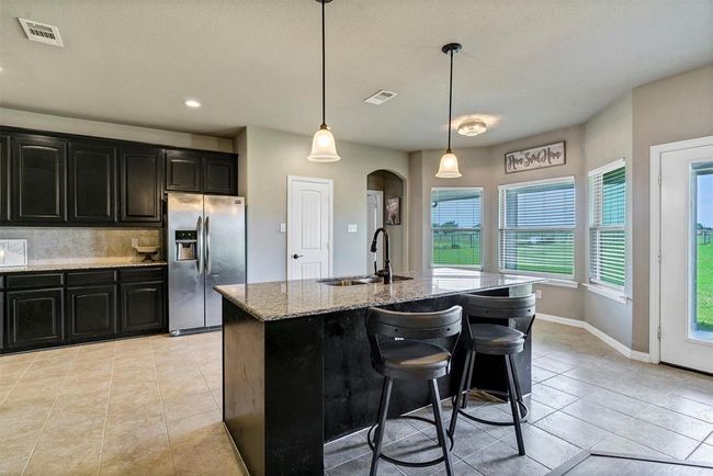 Kitchen with decorative light fixtures, backsplash, stainless steel refrigerator with ice dispenser, sink, and light tile floors | Image 10