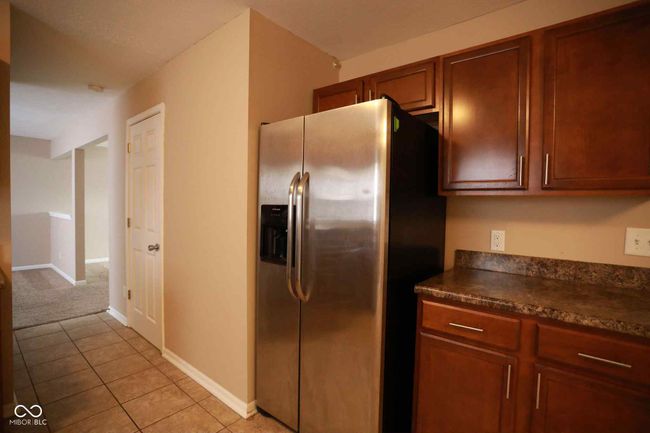 kitchen with dark countertops, baseboards, stainless steel fridge, light tile patterned flooring, and brown cabinetry | Image 19