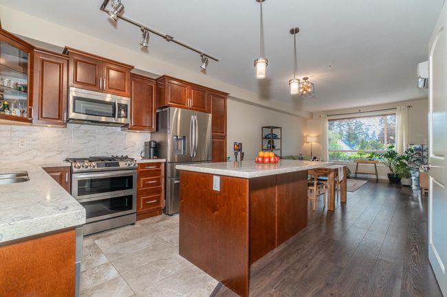 Kitchen featuring appliances with stainless steel finishes, pendant lighting, backsplash, glass insert cabinets, and a center island | Image 19