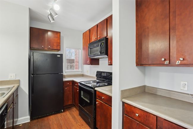 Kitchen with wood finished floors, a sink, black appliances, light countertops, and reddish brown cabinets | Image 4