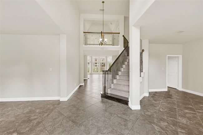 Inside, the foyer opens dramatically, where a graceful staircase sweeps upward and long sightlines draw the eye toward the sunlit main living spaces. | Image 5