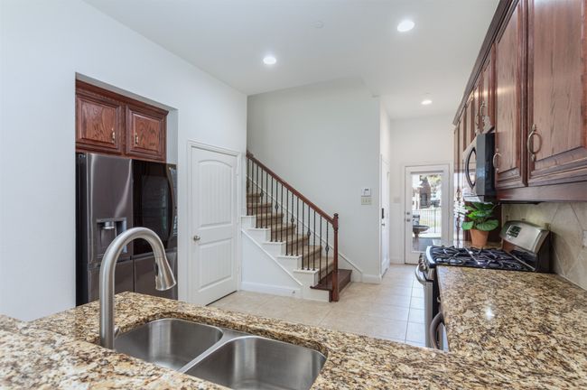Kitchen with light tile patterned floors, appliances with stainless steel finishes, light stone countertops, and a sink | Image 12
