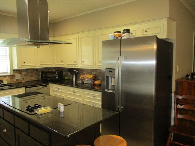 Kitchen featuring stainless steel fridge with ice dispenser, white cabinetry, white dishwasher, decorative backsplash, and island range hood | Image 17