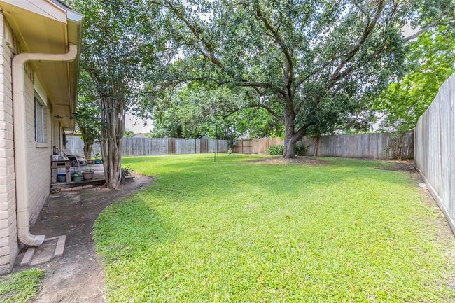Spacious backyard with lush grass, a large shade tree, and a wooden fence for privacy, offering a serene outdoor space. | Image 28