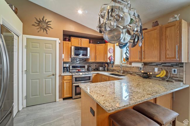 Kitchen featuring tasteful backsplash, light stone countertops, appliances with stainless steel finishes, a sink, and a peninsula | Image 7