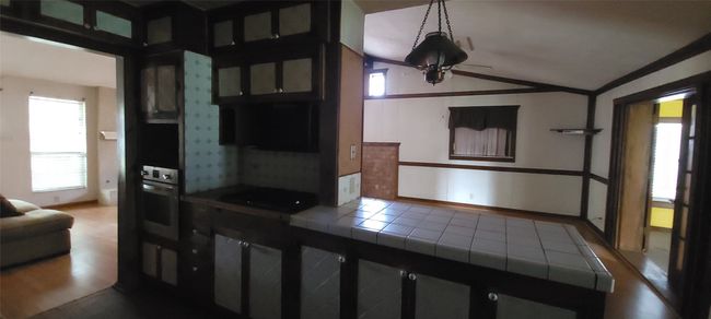 Kitchen featuring tile counters, oven, lofted ceiling, wood finished floors, and glass insert cabinets | Image 9