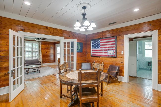 Dining space featuring french doors, wooden walls, a chandelier, light wood finished floors, and ornamental molding | Image 17