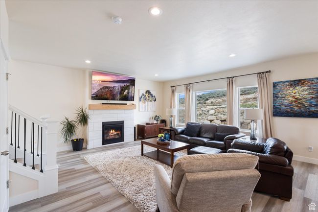 Living room with light wood-style floors, a tiled fireplace, recessed lighting, and stairway | Image 7
