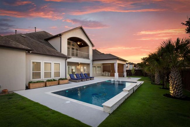 This heated pool sparkles under sunset skies, framed by manicured palms and an extended patio with a full summer kitchen and outdoor living for all seasons Texas living. | Image 40