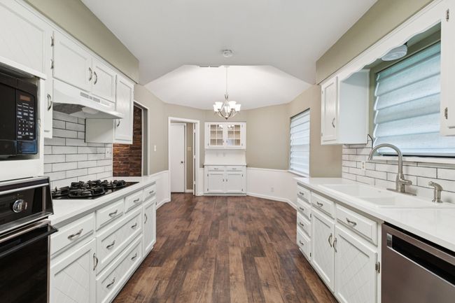 Kitchen featuring black appliances, under cabinet range hood, decorative backsplash, and a chandelier | Image 13
