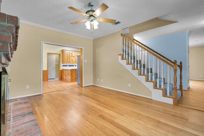 Unfurnished living room featuring light wood finished floors, ceiling fan, stairway, ornamental molding, and a textured ceiling | Image 4