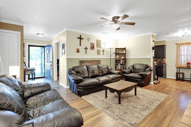 Living area featuring light wood finished floors, a ceiling fan, a textured ceiling, crown molding, and wainscoting | Image 15