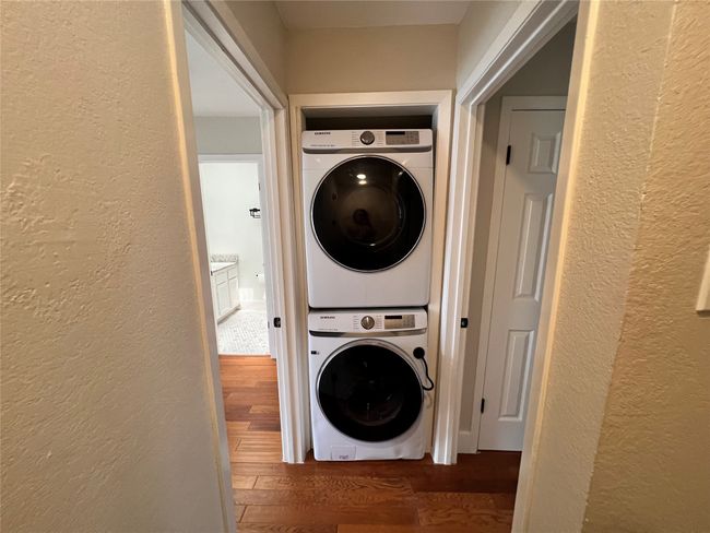 Clothes washing area featuring estacked washer and dryer, a textured wall, and wood finished floors | Image 19