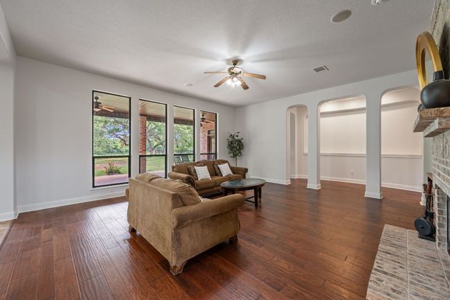 Living area featuring baseboards, arched walkways, dark wood finished floors, a brick fireplace, and a ceiling fan | Image 6