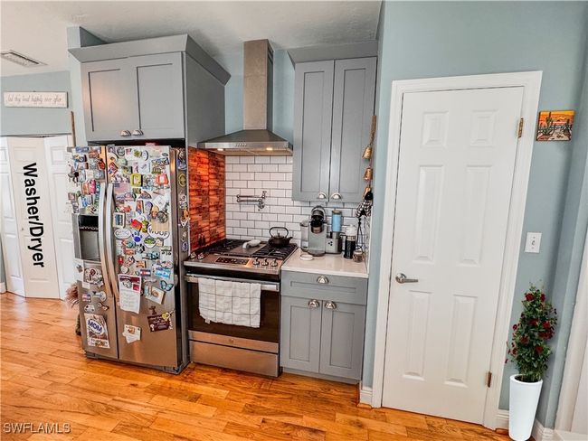 Kitchen featuring wall chimney range hood, tasteful backsplash, gray cabinets, light wood finished floors, and appliances with stainless steel finishes | Image 10