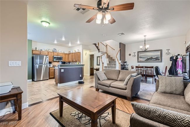 View of downstairs living space from corner of living room, with orientation of the kitchen, half bath and entry way to laundry room and garage, the stairway, a dining area and workspace in the background (behind the love seat and sofa) | Image 8
